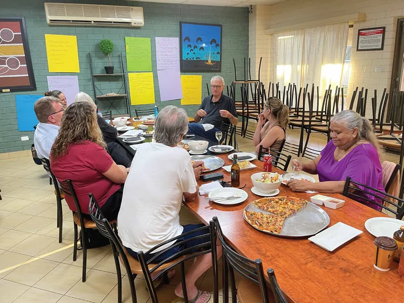 Community members talk around a table with shared food and workshop notes on the wall.