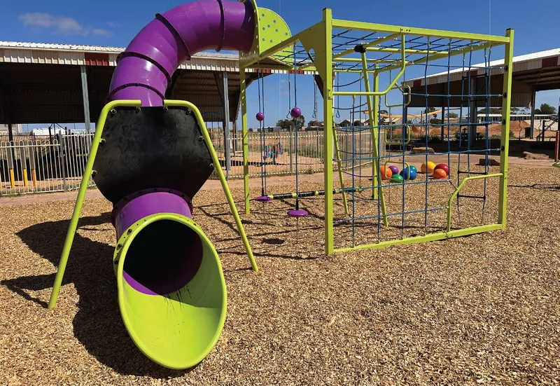 Purple slides and green climbing equipment in the shaded Coober Pedy playground.